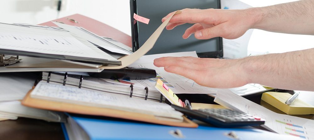 Businessman looking for his phone on his messy desk